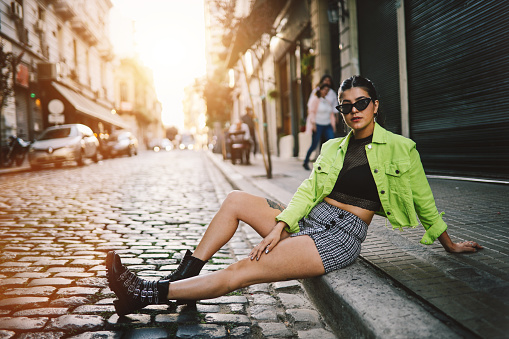 Young fashionable woman sitting and posing in the street, Buenos Aires, Argentina.