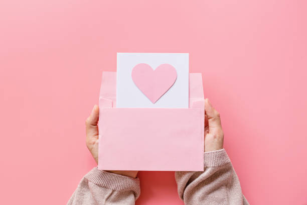 Valentine's day background. Female hands holding greeting card with pink hearth in envelope. Flat lay, top view, mock up, template, copyspace. Minimal abstract composition for 14 February celebration fondo del día de san valentín. manos femeninas sosteniendo tarjeta de felicitación con chimenea rosa en sobre. plano, vista superior, maqueta, plantilla, espacio de copia. composición abstracta mínima para la celebración del 14 de febrero
