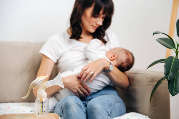 Mom gently looks at the baby and breastfeeds, next to the table is a breast pump for breast milk stock photo