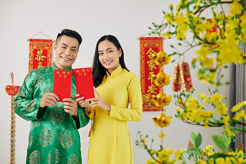Happy young Asian couple holding red envelopes, gifts for Lunar New Year and Tet celebration