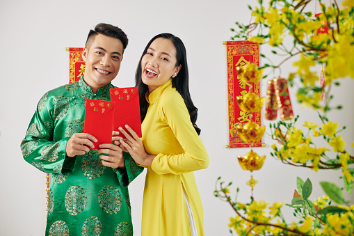 Joyful young couple showing red envelopes they are gifting family members and friends for Chinese New Year