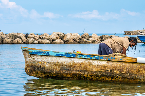 Montego Bay, Jamaica - March 19 2018: Jamaican male professional fisherman preparing motor boat for sailing to sea in early morning to catch fish and other seafood. Common work/ job in the Caribbean.