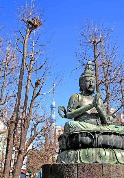 Asakusa, Tokyo, Japan on 29th March 2012. A bronze statue of Buddha at the Senso-ji Temple with workers in the background pruning tall trees.