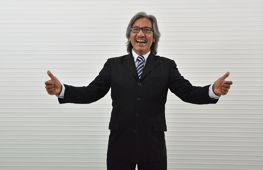 Cheerful elderly asian businessman in black suit and eyeglasses making thumbs up over white wall background, Business confident and success concept