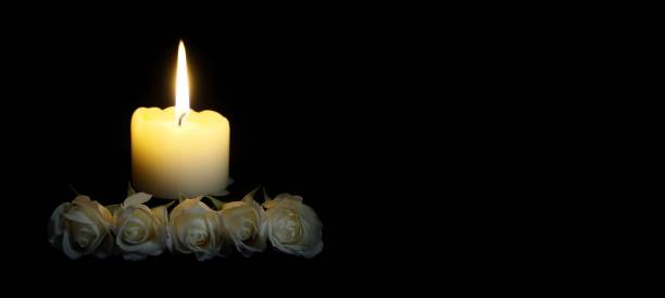 panoramic image of White roses and burning candles on table in darkness, Copy space for text. candles burning in the black background. Funeral symbol. The concept of mourn, grief or mourning.