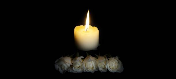 istock panoramic image of White roses and burning candles on table in darkness, Copy space for text. candles burning in the black background. Funeral symbol. The concept of mourn, grief or mourning. 1195521379