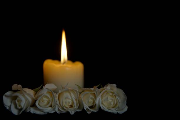 istock White roses and burning candles on table in darkness, Copy space for text. candles burning in the black background. Funeral symbol. The concept of mourn, grief or mourning. 1195521381