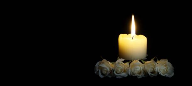 istock panoramic image of White roses and burning candles on table in darkness, Copy space for text. candles burning in the black background. Funeral symbol. The concept of mourn, grief or mourning. 1195521386