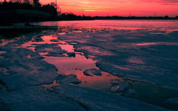 Sunset over water with broken pieces ice floating on surface near shore