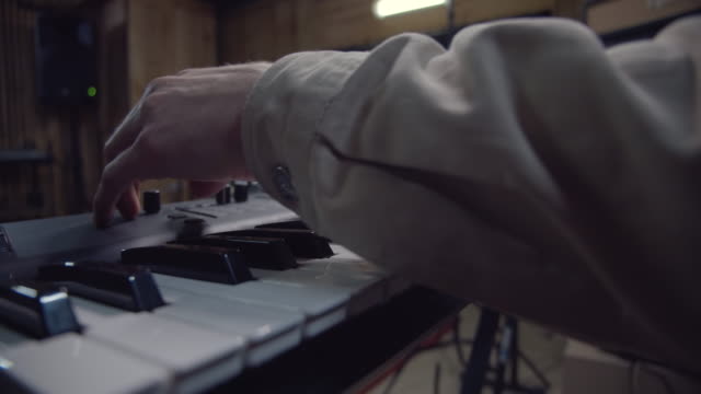Pianist turning controls and playing music on synthesizer, rehearsal in studio