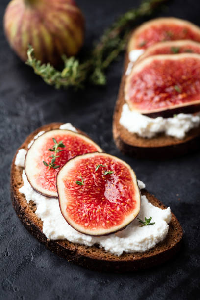Tasty rye bread toast with cream cheese and figs Tasty rye bread toast with cream cheese and fresh ripe figs. Healthy appetizer or snack. Black concrete background crostini stock pictures, royalty-free photos & images