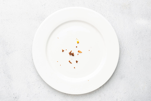 White plate with crumbs leftovers on grey concrete background. Top view