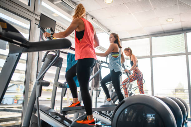 trois amis féminins d'entraînement utilisant des entraîneurs elliptiques - cross trainer photos et images de collection