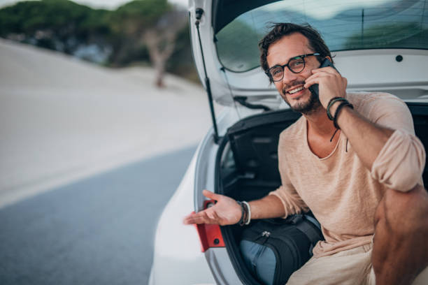 istock Guy sitting on car trunk and talking on mobile 1195554693