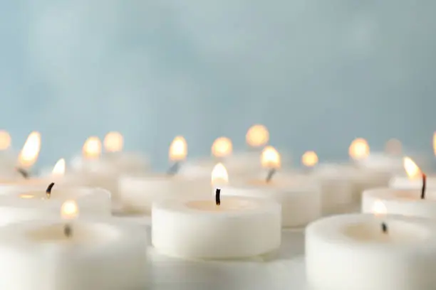 Photo of Group of burning candles against blue background, close up
