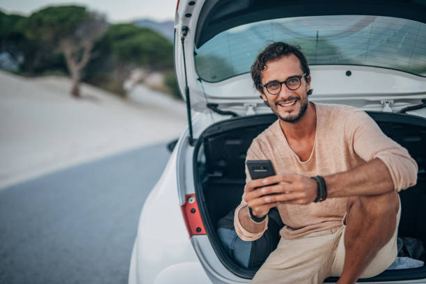 istock Young man sitting on car trunk 1195556835