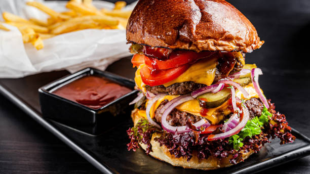 cocina americana. gran hamburguesa real con una chuleta de carne doble, tocino, tomates, pepinos, queso, cráneo, cebollas rojas y una salsa. copiar espacio, imagen de fondo - hamburger burger symmetry cheeseburger fotografías e imágenes de stock