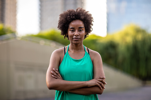 Portrait of serious Black female athlete with crossed arms, standing outdoor , looking at camera