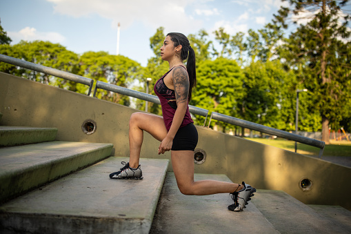 Latin  woman in sports wear stretching after training session at park on stairs, side view