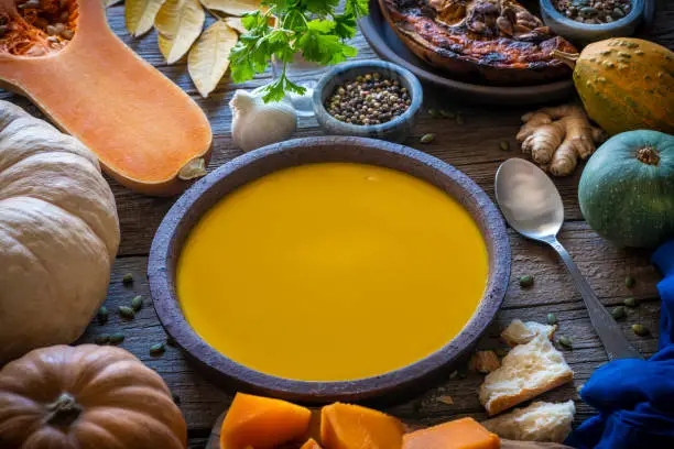 Autumn pumpkin soup and ingredients on rustic wooden table