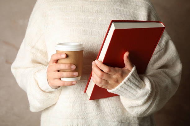 istock Woman holding book and coffee against brown background, front view 1195564010