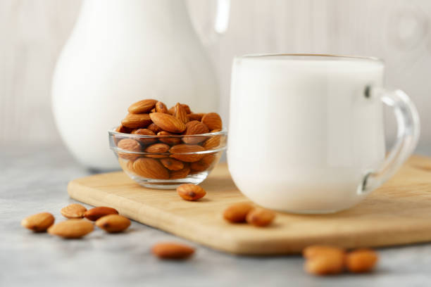 latte di mandorla in una brocca di vetro e tazza, accanto a noci in una ciotola su uno sfondo di cemento. - almond bowl ceramic food foto e immagini stock