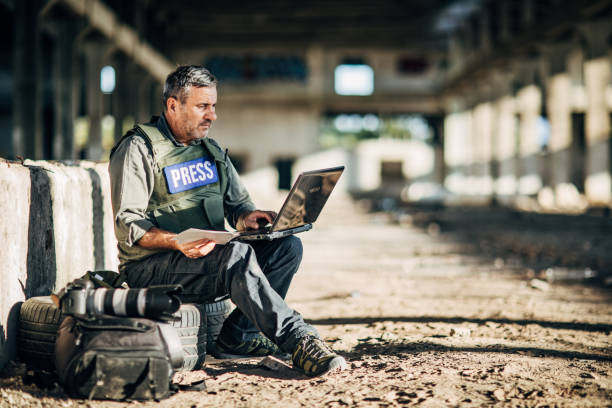 Mature man war journalist using laptop in abandoned building One man, war journalist with using laptop at the place of action, in war zone. journalist photos stock pictures, royalty-free photos & images