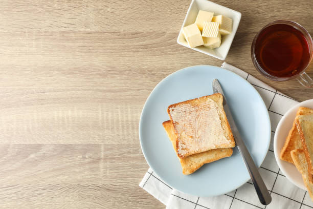 toasts on plate, towel, tea and butter on wooden background, copy space - butter toast bread breakfast imagens e fotografias de stock