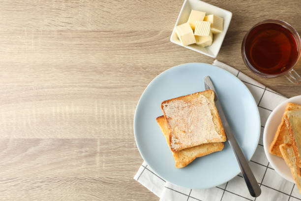 тосты на тарелке, полотенце, чай и масло на деревянном фоне, копия пространства - butter toast bread breakfast стоковые фото и изображения