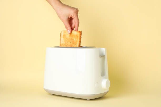 istock Female hand puts bread in a toaster on beige background, space for text 1195568457