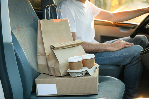 Blank box, coffee cups, paper packages and courier in car. Delivery
