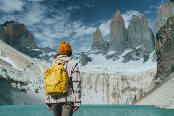 Woman with yellow backpack looking  at scenic view of Torres del Paine National Park stock photo
