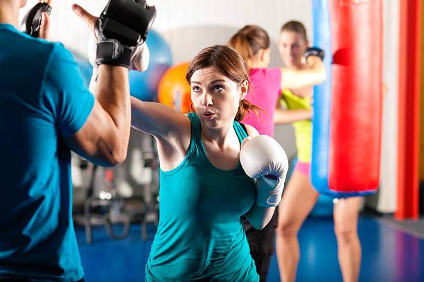 Female kick boxer with trainer in sparring Woman Boxer hitting the sandbag, her trainer is assisting kickboxing photos stock pictures, royalty-free photos & images