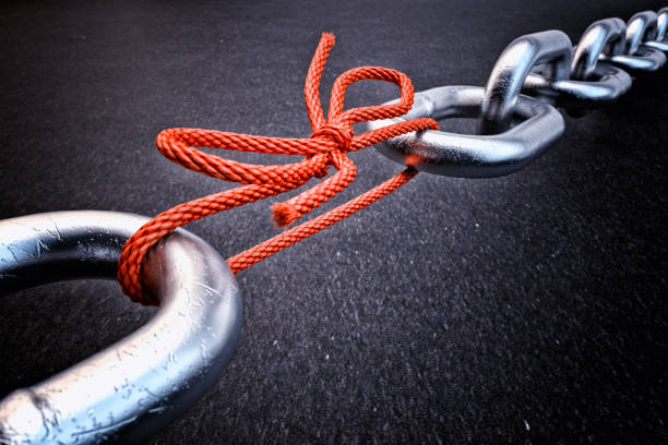 Weakest link, security break fix and strength concept Metallic chain connected by a red knotted rope on black background weakness stock pictures, royalty-free photos & images