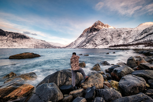 Seascape with snow mountain and photographer standing on rock at coastline, Segla, Northern Norway