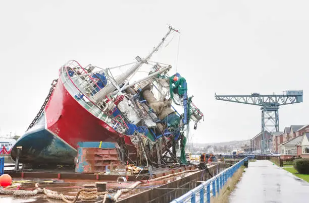 Capsized ship vessel and rescue lift crane at port dock for repair of shipwreck uk