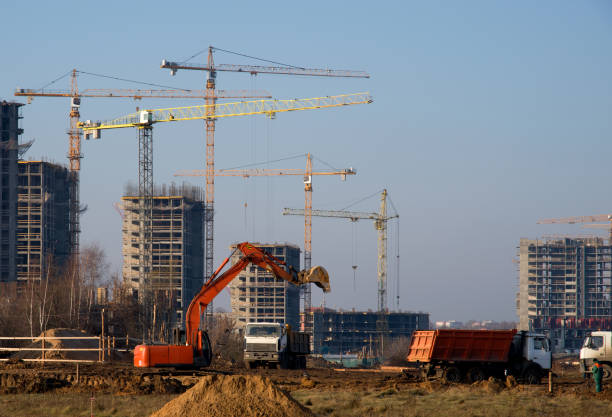 istock Excavator at a construction site on a background of a construction cranes and building. Backhoe dig the ground for the foundation, laying storm sewer pipes. Installation of water main systems. 1195581517
