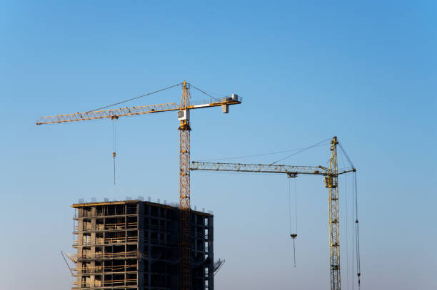 istock Tower cranes constructing a new residential building at a construction site against blue sky. Renovation program, development, concept of the buildings industry. 1195583828