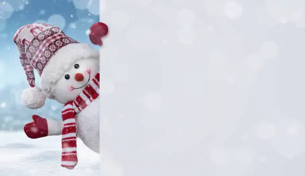 Photo of Happy snowman behind blank banner with copy space