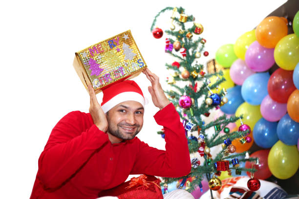 Young handsome men with carrying Christmas gifts on head and he looks so happy, celebrating and enjoying merry Christmas at home.