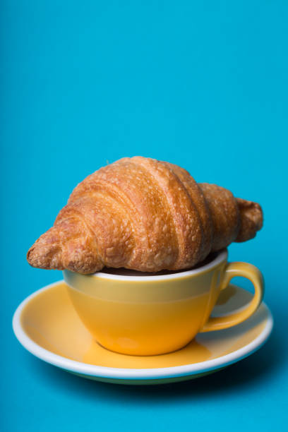 beautiful coffee yellow cup with  cappuccino and croissant on blue background\