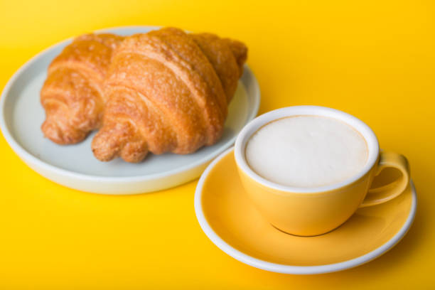 beautiful coffee yellow cup   cappuccino with croissant on yellow background\