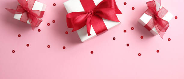 istock Valentine's Day banner with white gift boxes decorated red ribbon bow on pink background with confetti. Flat lay, top view. 1195585732