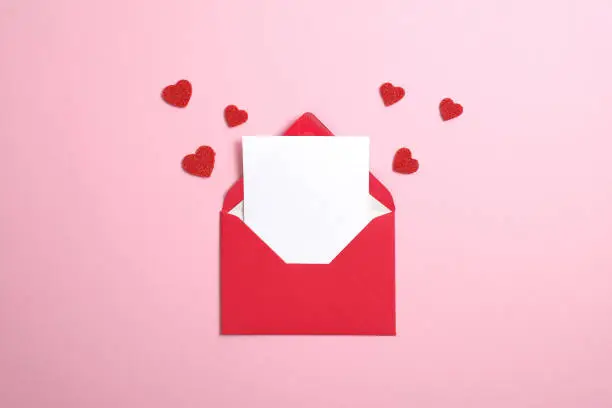 Photo of Red paper envelope with blank white note mockup inside and Valentines hearts on pink background. Flat lay, top view. Romantic love letter for Valentine's day concept.