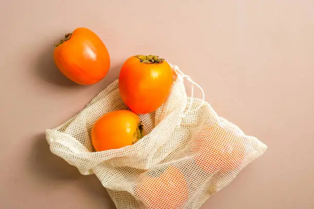 Zero waste fishnet bag with persimmons. Eco friendly products, plastic free concept. Sustainable lifestyle. Flat lay, top view.