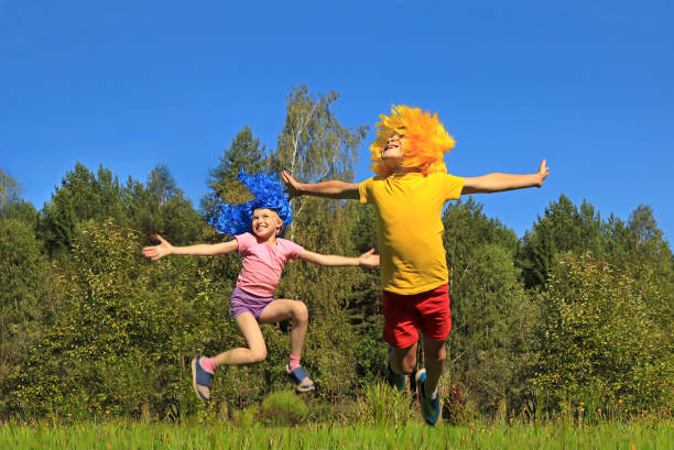 bambini gioiosi ragazzo e ragazza con i capelli blu e gialli che saltano sul prato in natura - arms raised green jumping hand raised foto e immagini stock