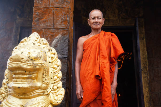 Khmer buddhist monk standing near a Singha Khmer statue. Kampot, Cambodia - SEPTEMBER 22, 2013: Khmer buddhist monk standing near a Singha Khmer statue and looking at the camera. Wat Sampov Pram. kampot stock pictures, royalty-free photos & images