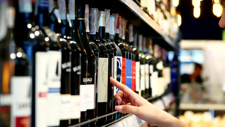 Woman chooses wine in the Supermarket, customer selects product on the shelves in the store in close-up