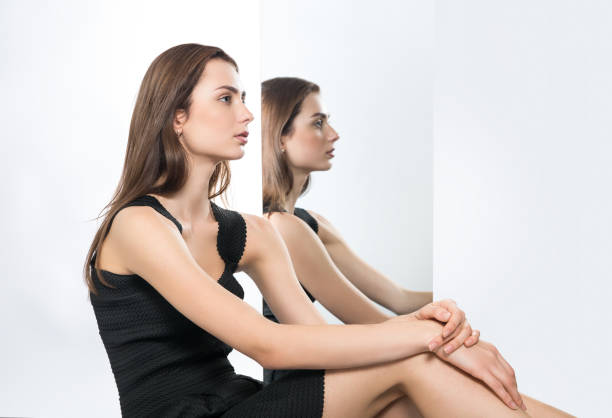 young beautiful girl in the Studio and its reflection in the mirror. Black dress. Light grey background