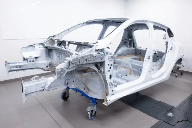 Custom car being build in workshop. Sports car body, car frame is assembled by mechanics. Metallic auto chassis in the air, car skeleton in service